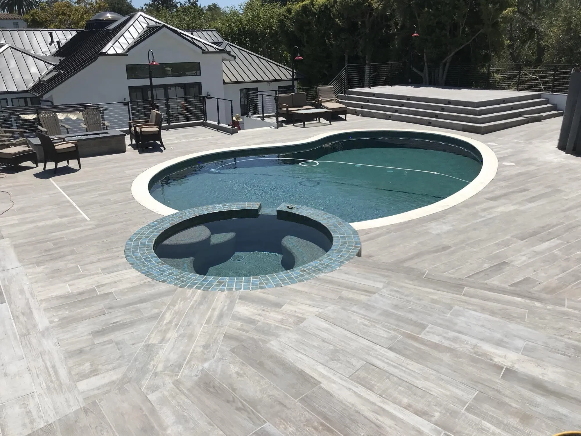 Finished freeform pool and raised spa on an elevated hillside deck with tree-lined views