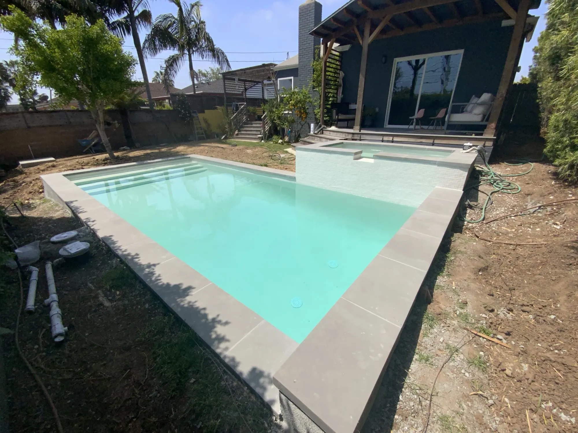 Finished backyard pool with raised spa, tile spillover, paver deck and palm trees