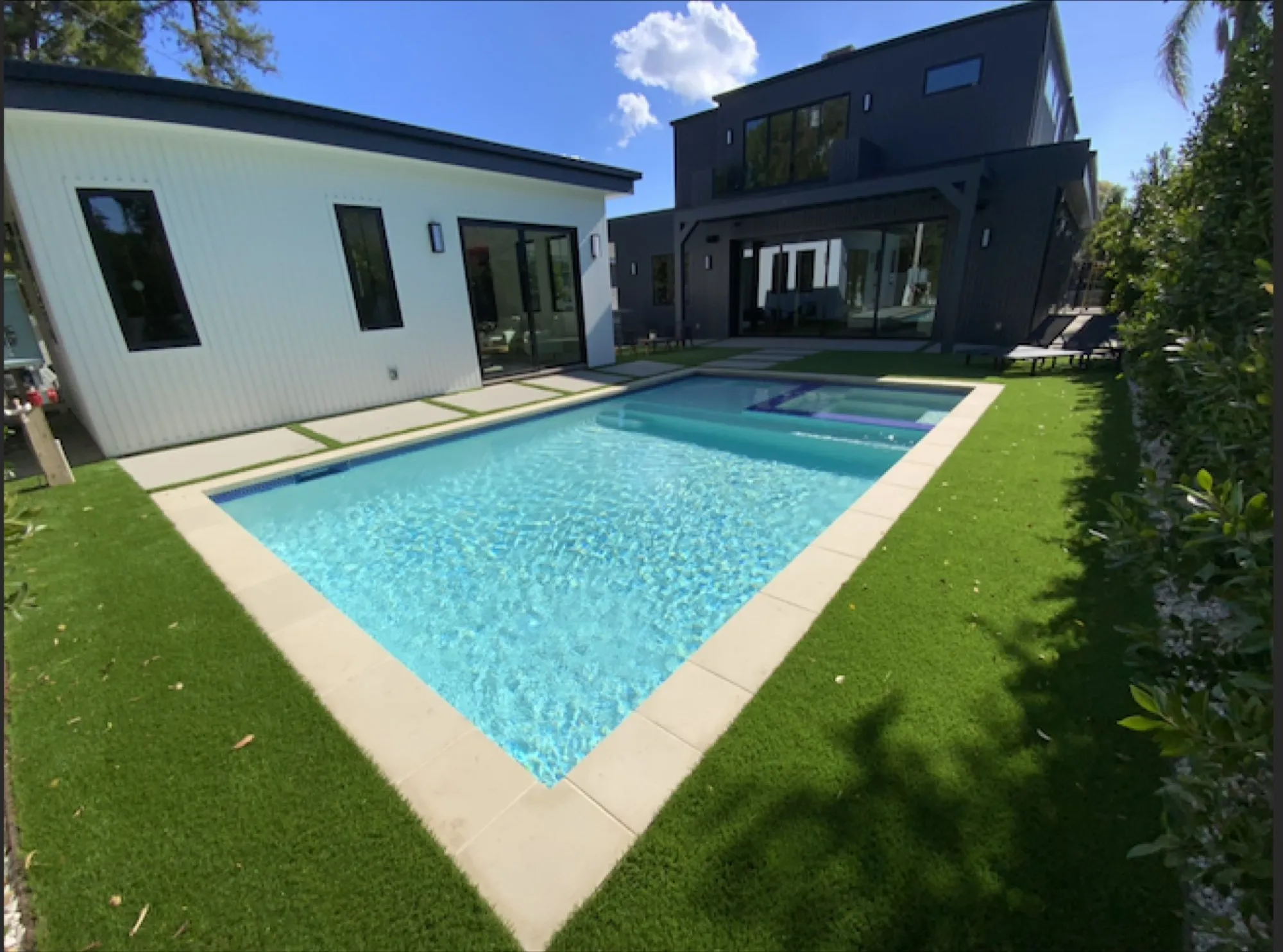 Finished rectangular pool and spa on turf in front of a modern black-and-white two-story house