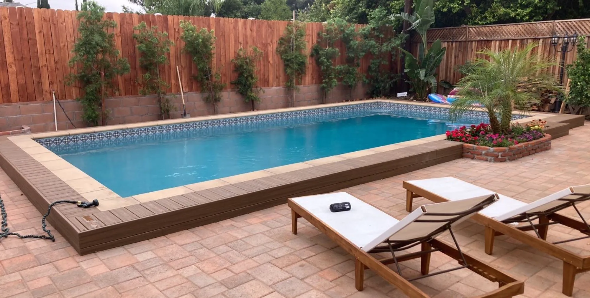 After: finished rectangular pool with decorative Talavera-style waterline tile, a paver patio and a raised wood platform at the water's edge