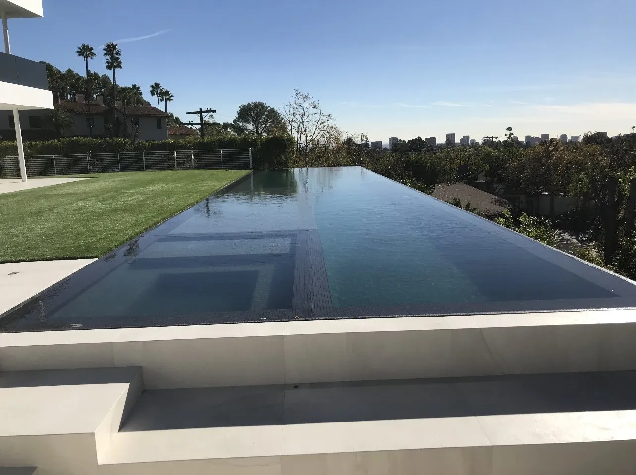 After: Finished modern infinity-edge pool on a hillside terrace with a city skyline view.