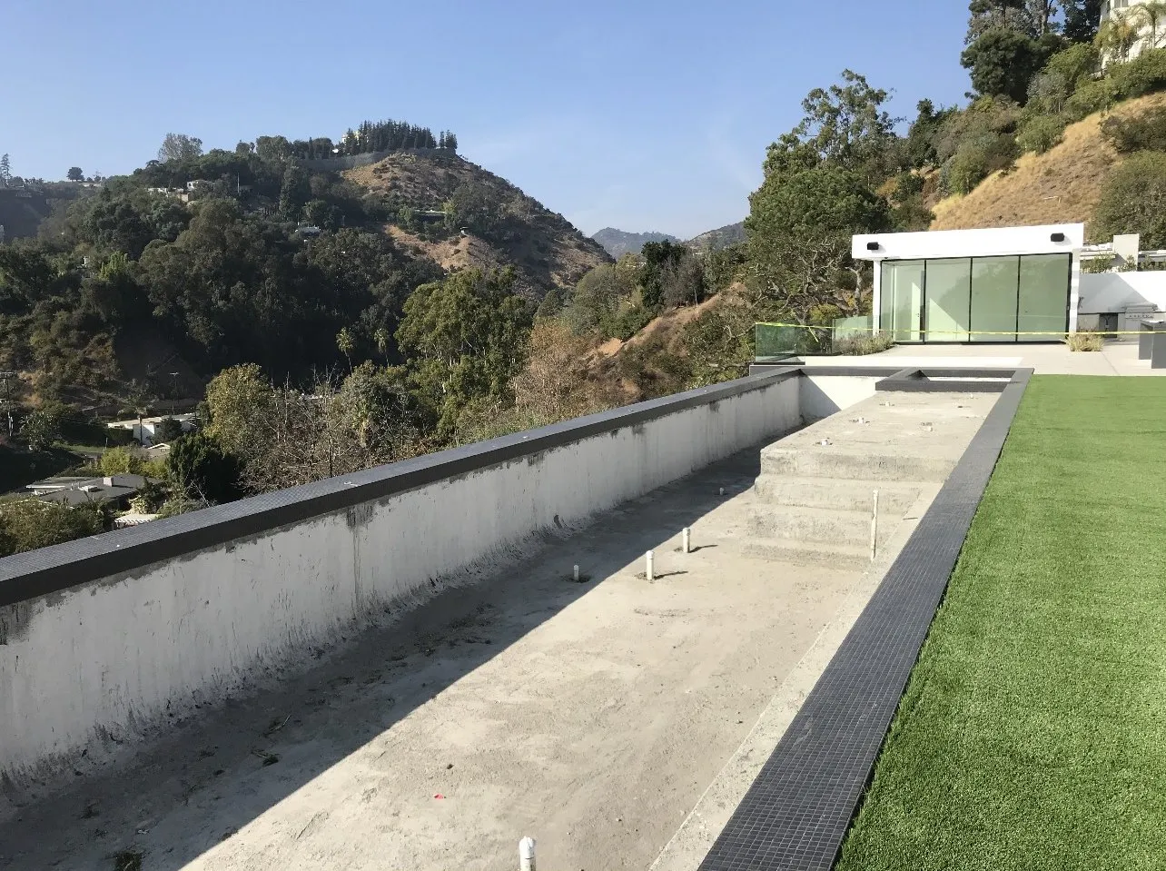 Before: Unfinished concrete pool shell on a rooftop terrace with glass railing.