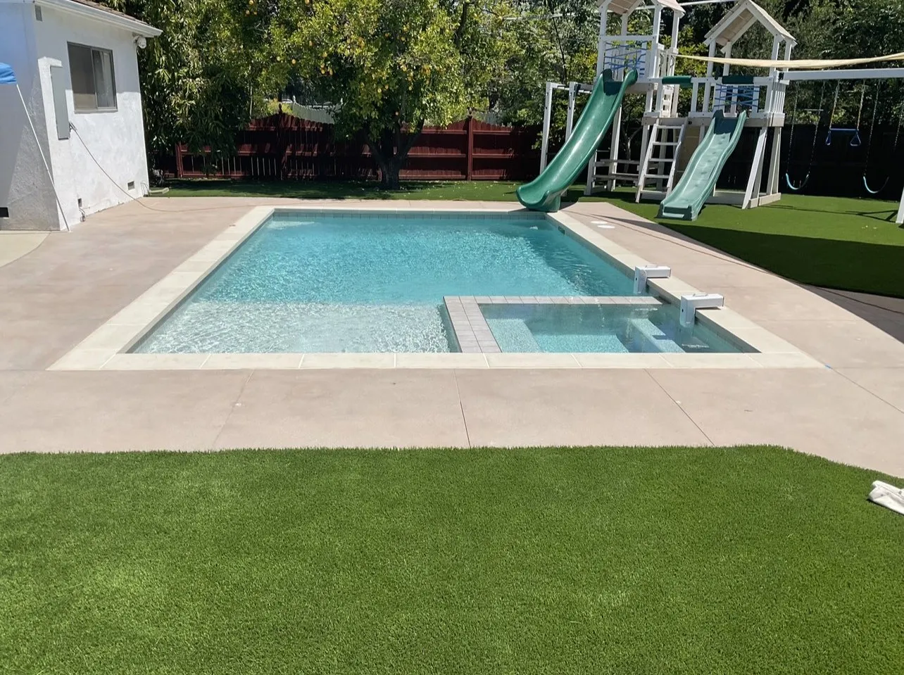 After: Finished family pool with a tanning ledge and a play-structure slide alongside.