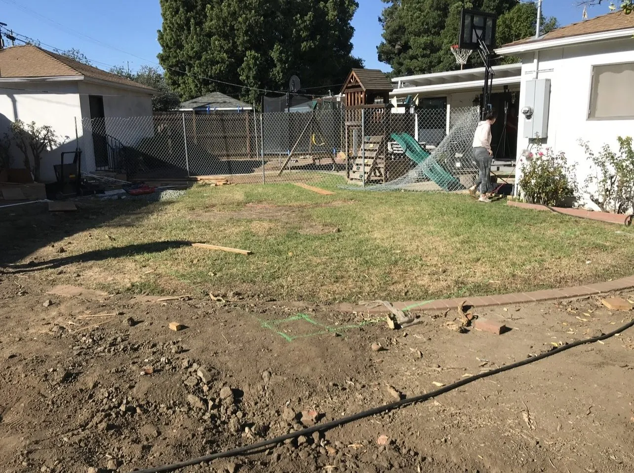 Before: Fenced-in backyard with a children's play structure and no pool yet.