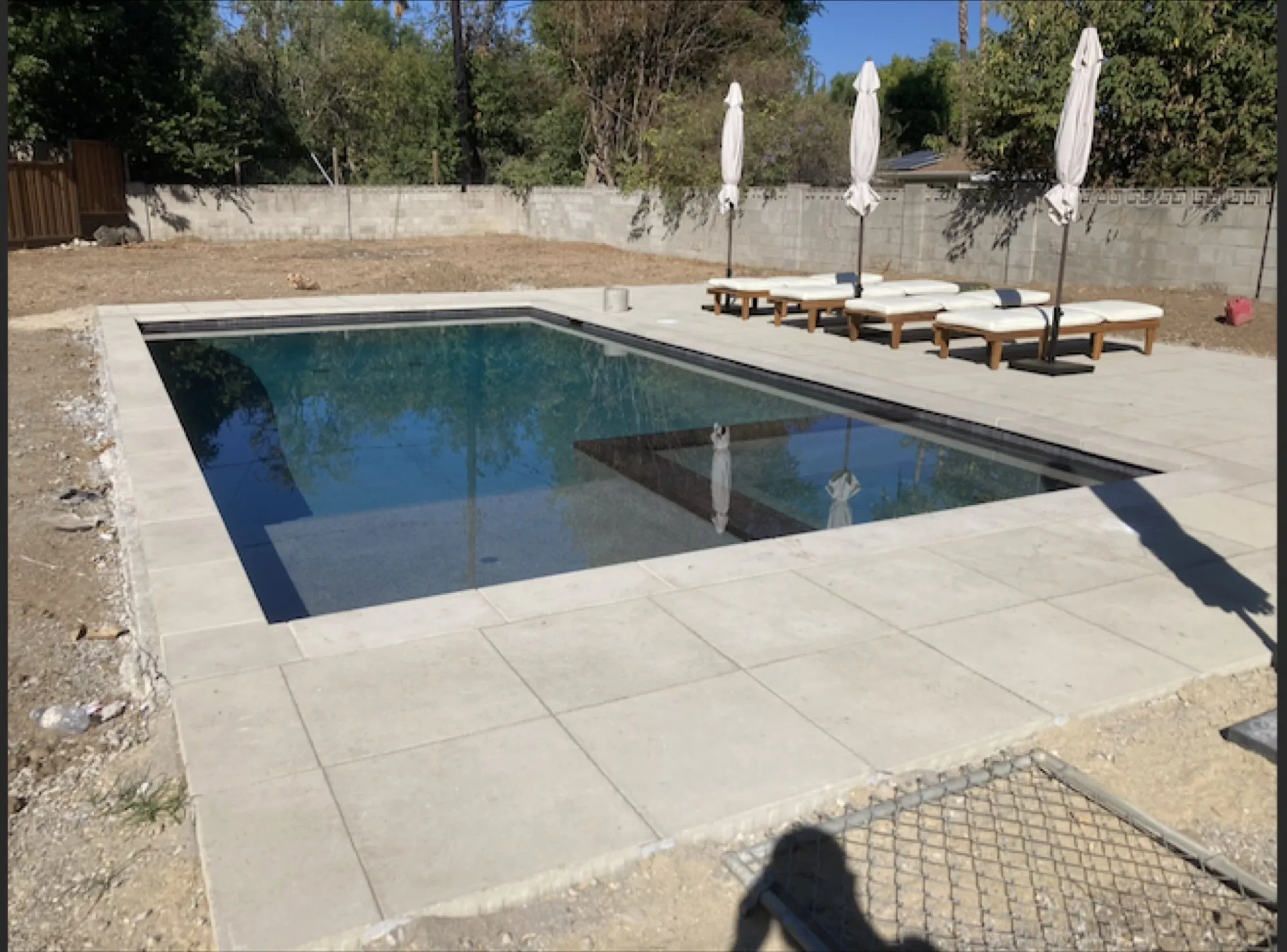 Finished dark-tile pool with lounge chairs and umbrellas on a stone deck