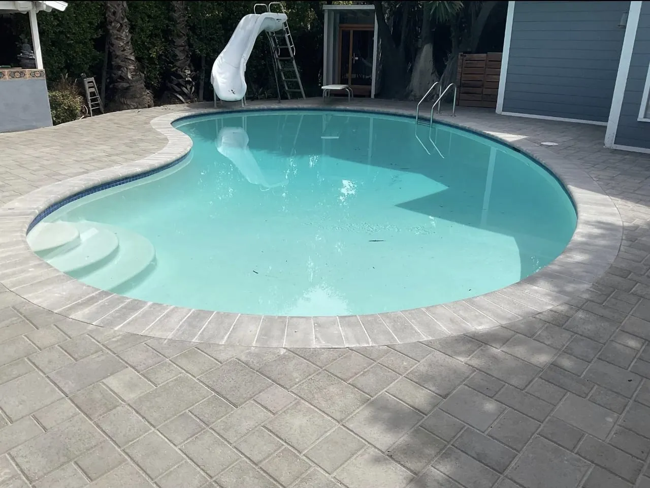 After: Refinished kidney pool with light blue water and paver deck.