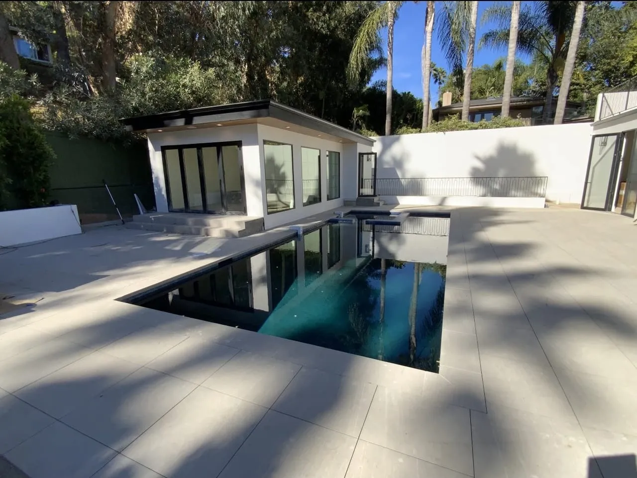 After: Finished modern pool and raised spa framed by large gray pavers.