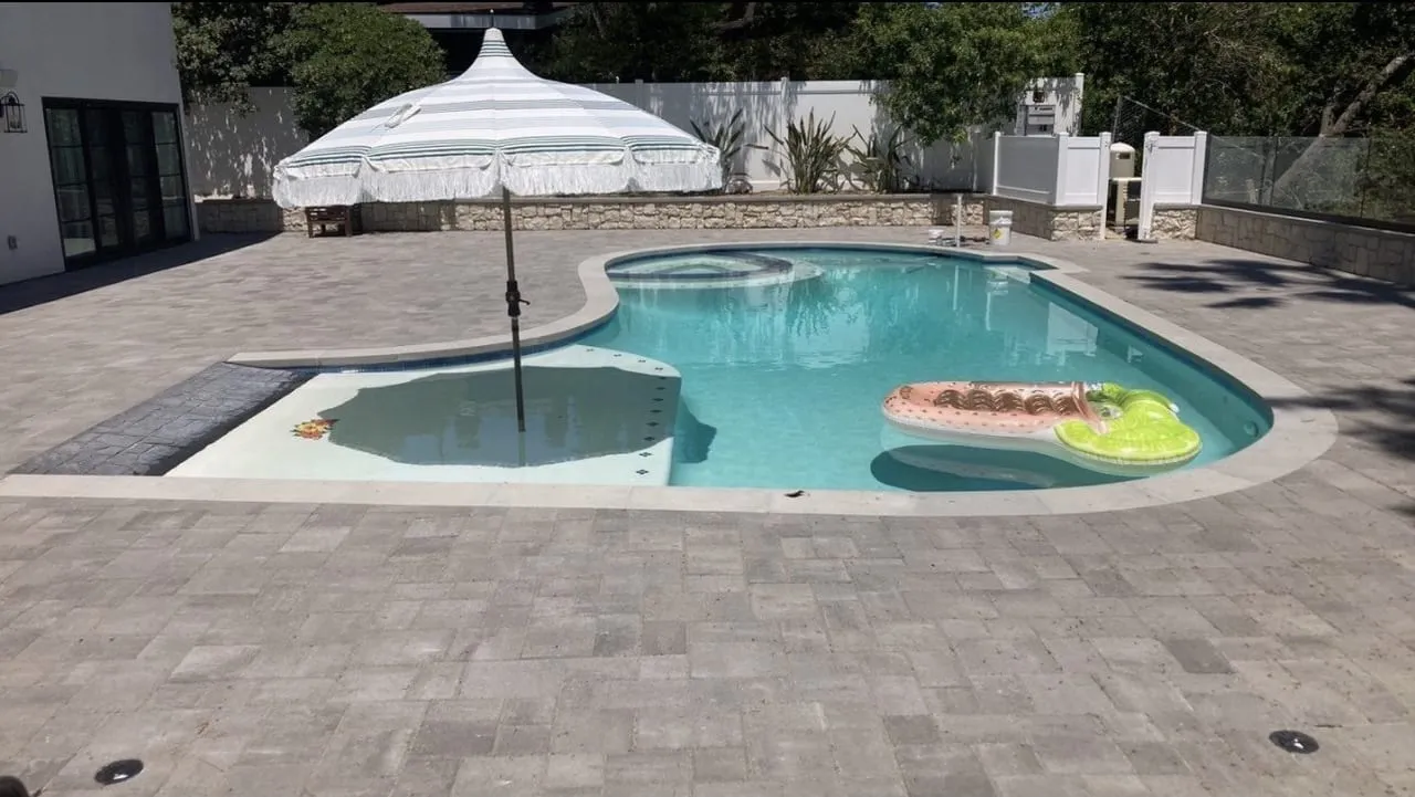 After: Finished free-form pool with paver deck, umbrella, and floats.